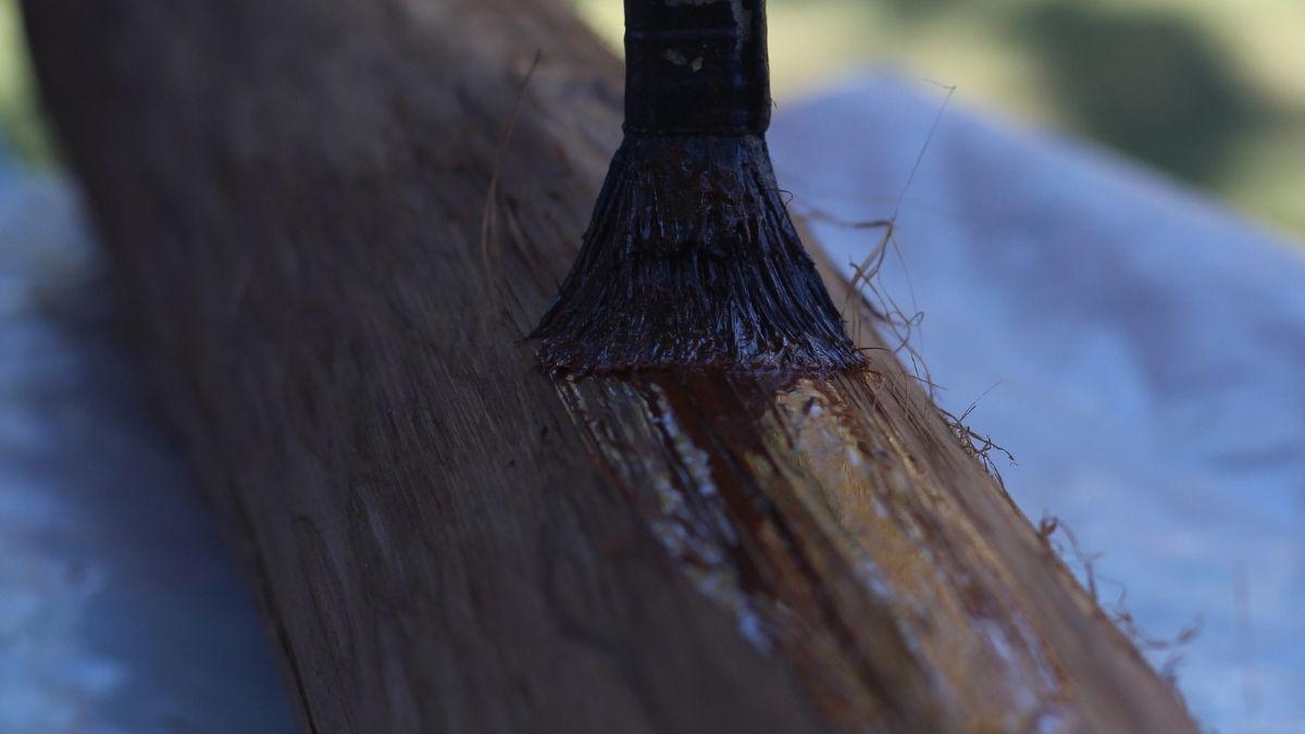 A paint brush applying wood hardener to a piece of wood