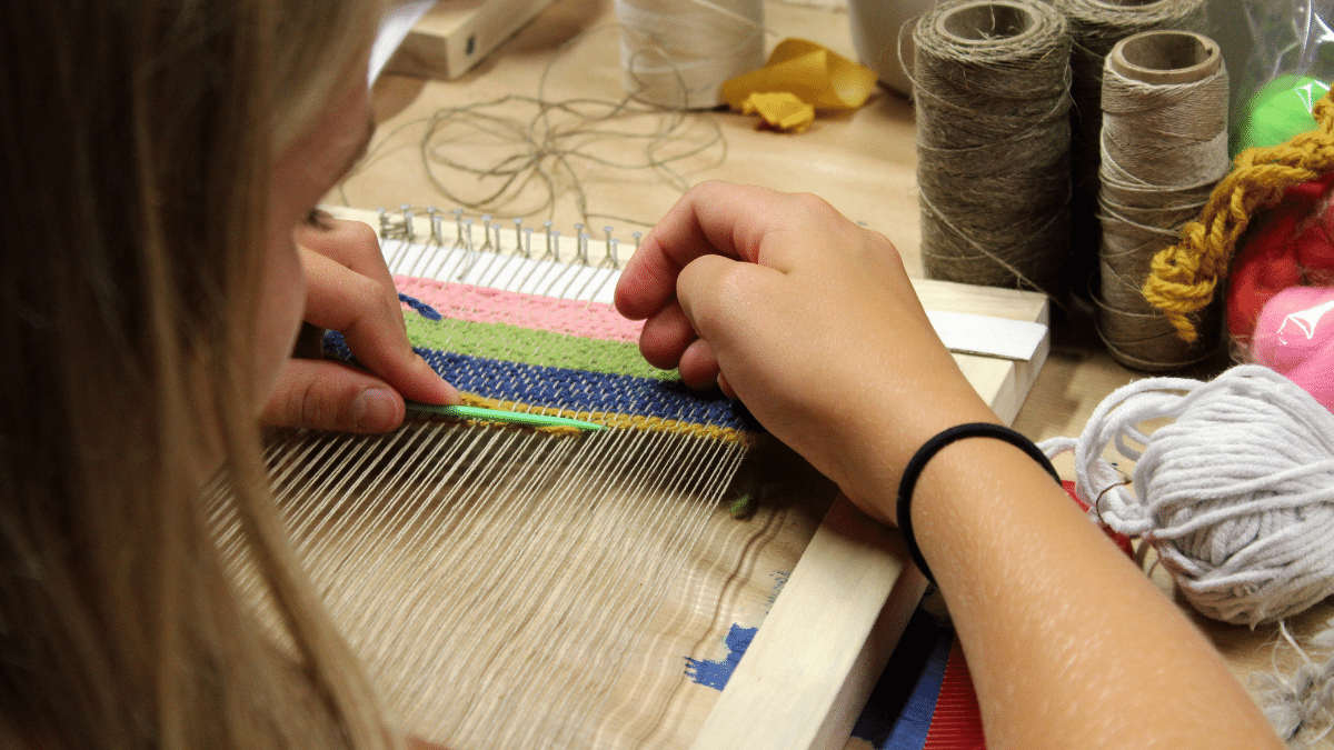 close up of young woman weaving a multi coloured pattern