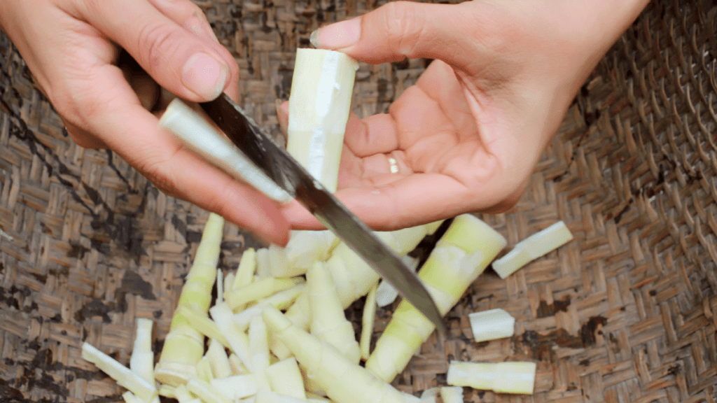 close up of female hands using a knife to cut bamboo shoots into a basket