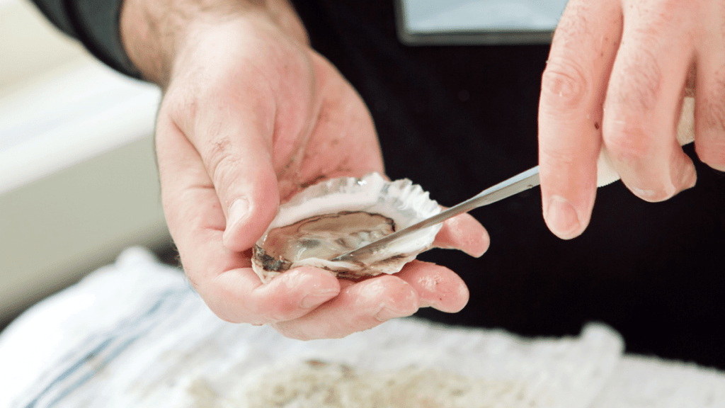 man removing oyster from shell using a knife